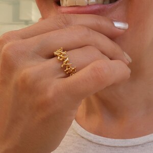 May include: A gold ring with a delicate, intricate design. The ring is made of small, interconnected pieces of metal that create a unique and eye-catching pattern.