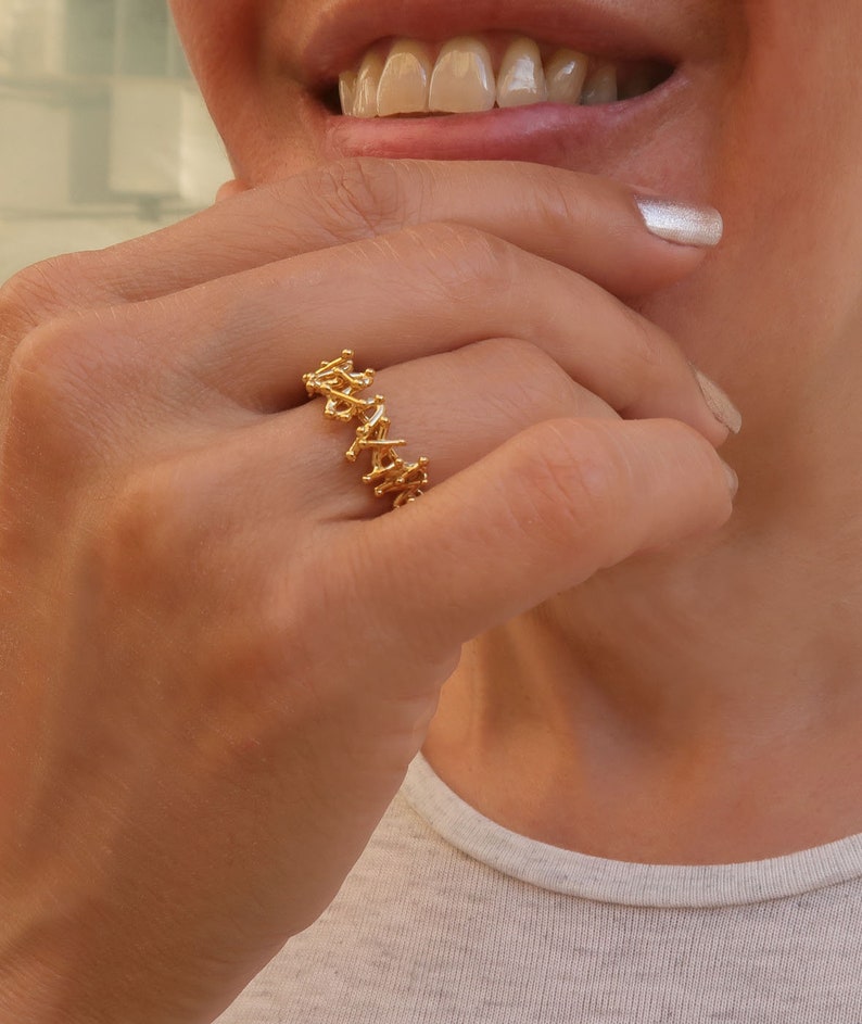 May include: A gold ring with a delicate, intricate design. The ring is made of small, interconnected pieces of metal that create a unique and eye-catching pattern.
