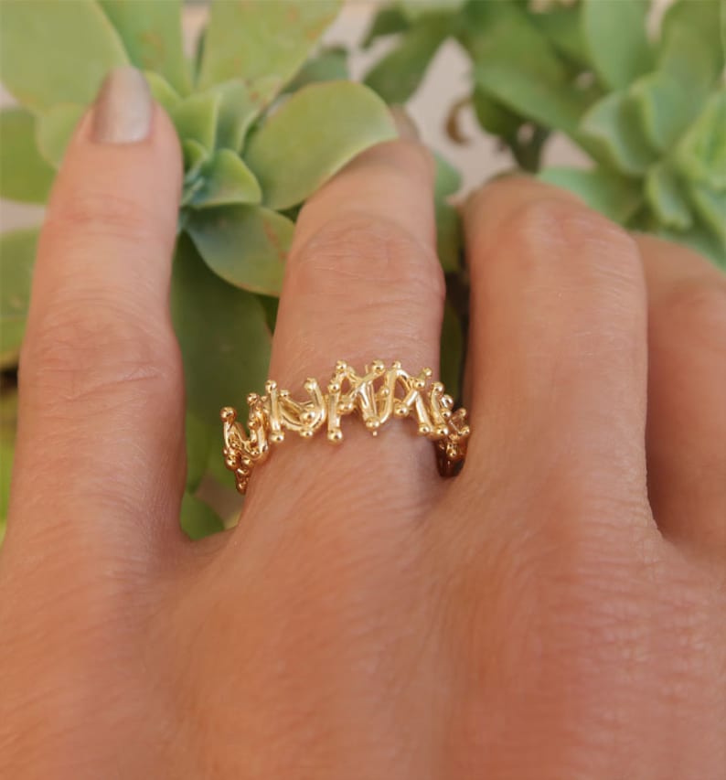 May include: A gold ring with a delicate, intricate design. The ring is made of small, interconnected loops and circles, creating a unique and modern look.