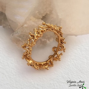 May include: A gold ring with a unique, intricate design resembling a delicate, organic pattern. The ring is made of small, interconnected circles and lines, creating a textured and visually interesting piece.