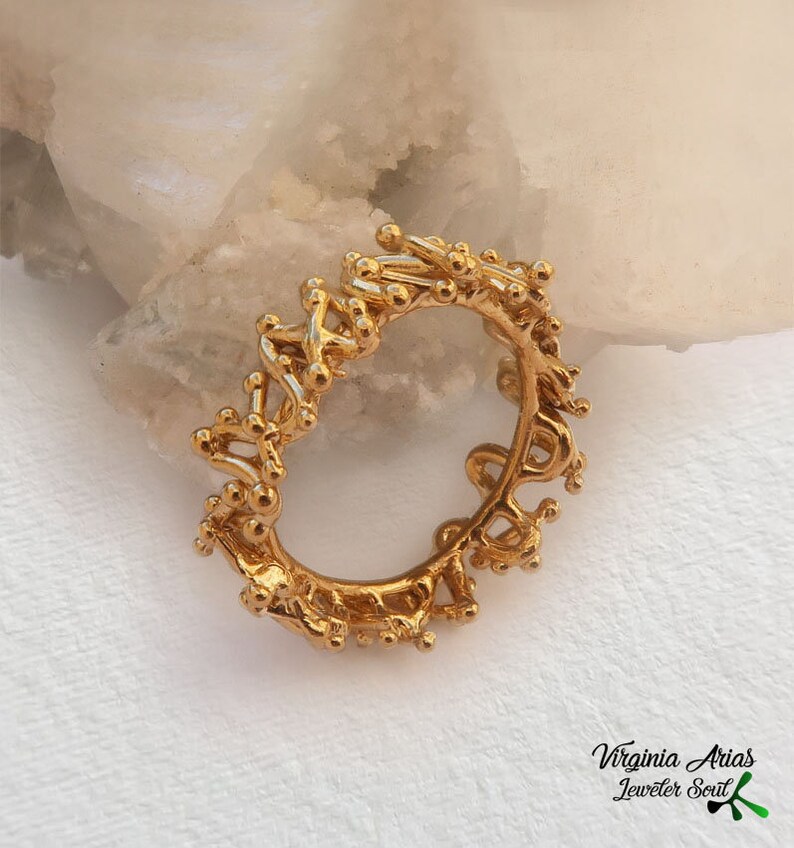 May include: A gold ring with a unique, intricate design resembling a delicate, organic pattern. The ring is made of small, interconnected circles and lines, creating a textured and visually interesting piece.