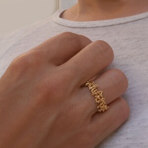 May include: A gold ring with a delicate, intricate design. The ring is made of a thin band of gold and features a pattern of small, interconnected loops and swirls.