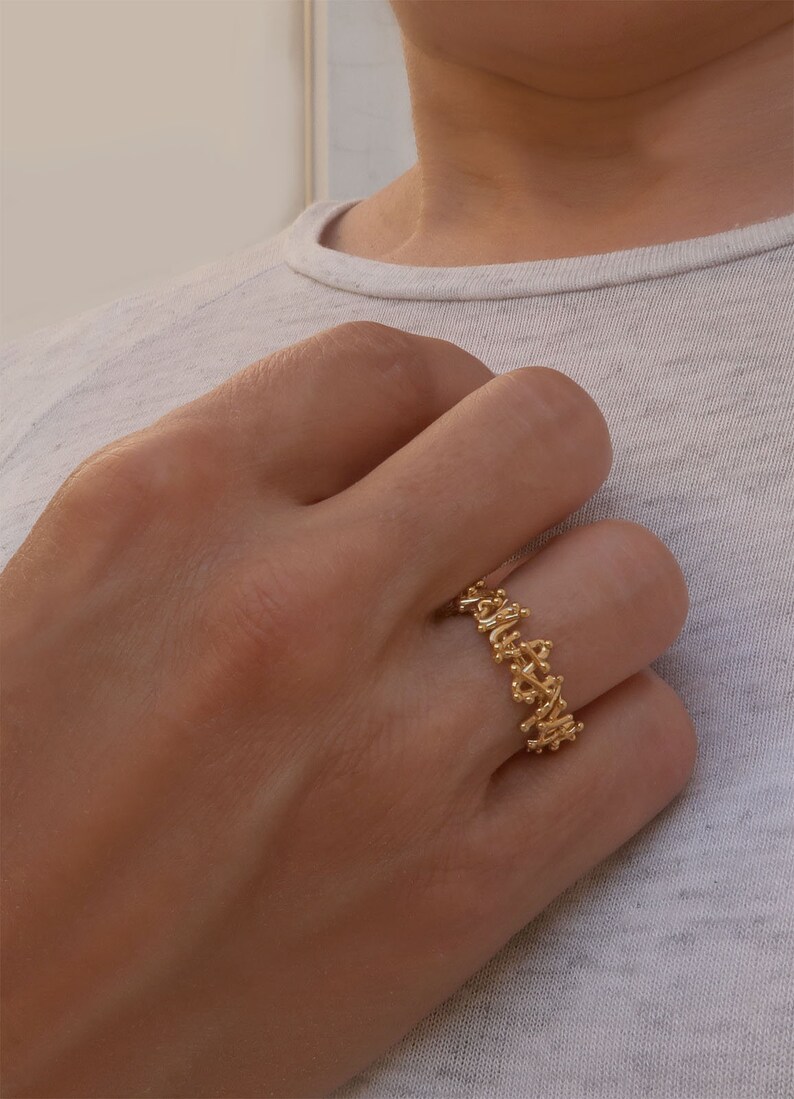 May include: A gold ring with a delicate, intricate design. The ring is made of a thin band of gold and features a pattern of small, interconnected loops and swirls.