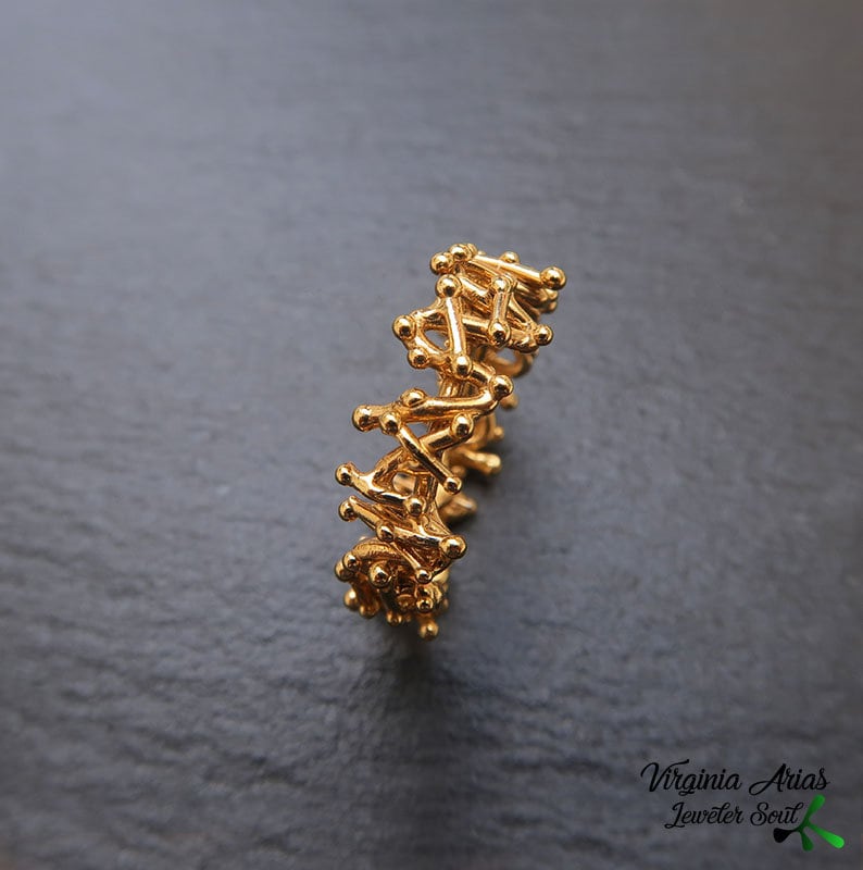 May include: A gold ring with a unique, intricate design made of small, interconnected pieces. The ring is made of a single piece of metal and has a delicate, airy feel.