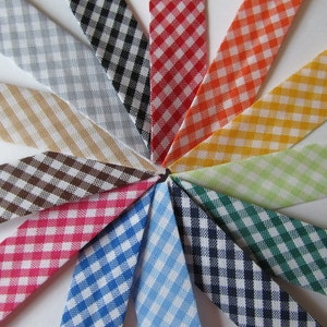 May include: A selection of gingham ribbons in a circular arrangement. The ribbons showcase a range of colours, such as green, blue, pink, brown, and yellow, each with a traditional checkered pattern. The ribbons are made of fabric.