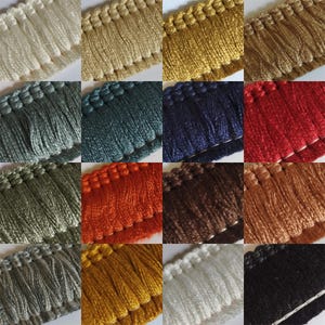 May include: A selection of decorative fringe trim in a variety of colours. The colours include cream, gold, olive green, teal, navy, red, orange, brown, tan, grey, yellow, white, and black. Each trim has a looped top edge and a fringe of soft threads.