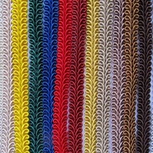 May include: A selection of decorative trim in a variety of colours, such as white, yellow, red, and blue. Each trim has a repeating, ornate pattern. The trims are arranged vertically, displaying a range of shades and textures.