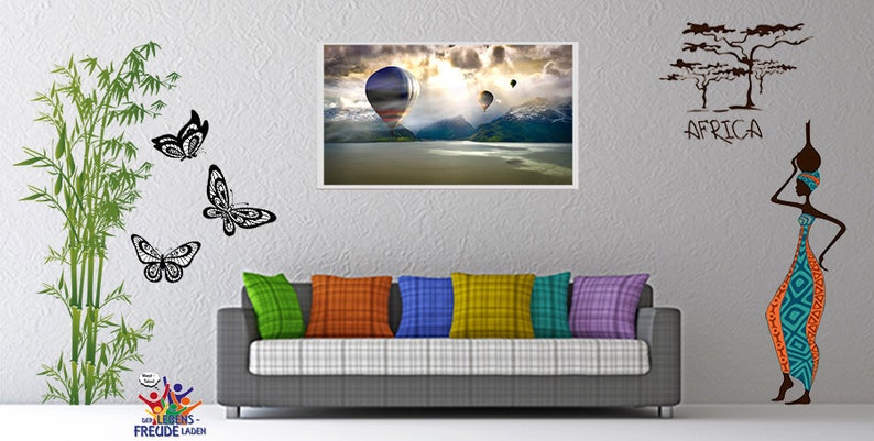 May include: A living room interior with a gray couch, colorful throw pillows, and wall decor. The wall decor includes a framed print of hot air balloons over a lake, a bamboo plant with butterflies, and a silhouette of a woman with a water jug, with the word "AFRICA" written above her.