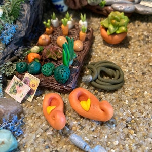 Puede incluir: Una escena de jardín en miniatura con una variedad de plantas, verduras y accesorios. Hay pequeñas zanahorias, cebollas y rábanos en una maceta de madera. También se incluye una manguera verde, una pala pequeña y dos zapatos naranjas.