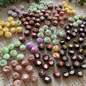 May include: Assortment of miniature polymer clay cupcakes with various toppings, including fruit, flowers, swirls, and rainbows. The cupcakes are arranged in rows on a woven surface.