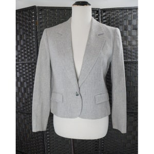 Pode incluir: Um blazer cinza com um único botão de fecho e lapela de entalhe. O blazer tem um caimento justo e é feito de um tecido texturizado.