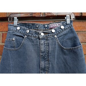 May include: A pair of high-waisted blue denim jeans with silver button closures and a "Gasson" label on the right side. The jeans have a classic five-pocket style.