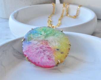 Peut inclure: Un collier en chaîne dorée avec un grand pendentif rond en agate multicolore. Le pendentif a un centre blanc avec des nuances de rose, jaune, vert et bleu.