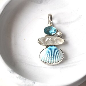Peut inclure: Un pendentif en argent avec une coquille de mer bleue et blanche, un cristal de quartz clair, une pierre précieuse bleue et une perle blanche.