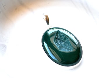 May include: A dark green oval pendant with a silver bail. The pendant features a sparkly, light green crystal inside.