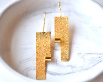 Puede incluir: Un par de pendientes de oro con un diseño rectangular texturizado y un pequeño acento de cilindro de oro.