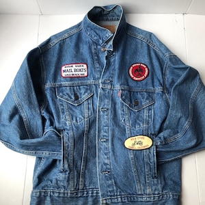 May include: A blue denim jacket with three patches. The patches are for "Rogue River Mail Boats Gold Beach Ore.", "Rock Store Coquille California", and "Black River Road Scenic Byway County Seat".