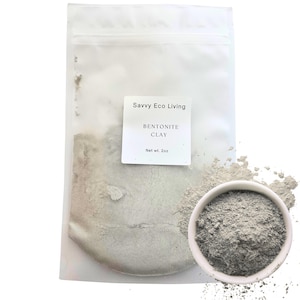 May include: A translucent plastic pouch containing grey bentonite clay powder with a white label reading Savvy Eco Living BENTONITE CLAY Net wt. 2oz. Next to the pouch is a small white bowl filled with the same fine grey clay powder.