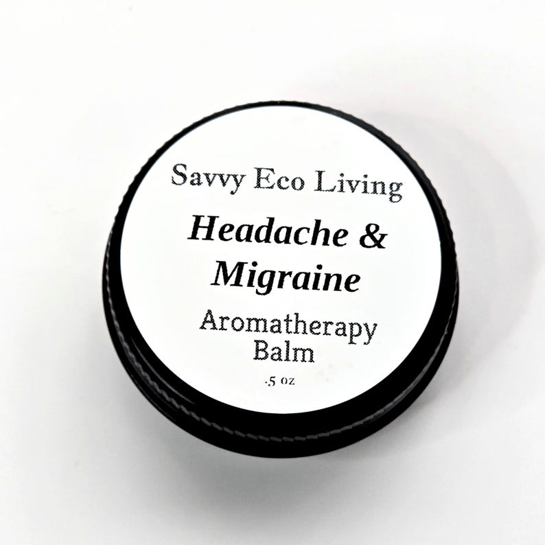 K&ouml;nnte beinhalten: Ein schwarzer, runder Beh&auml;lter mit wei&szlig;em Deckel. Der Deckel tr&auml;gt den Text "Savvy Eco Living Headache & Migraine Aromatherapy Balm" in Schwarz. Das Etikett gibt auch an, dass der Balsam 14 Gramm enth&auml;lt.