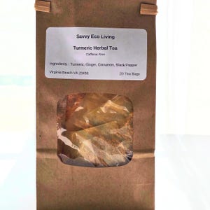 May include: A brown paper bag of Turmeric Herbal Tea from Savvy Eco Living. The label lists ingredients: Turmeric, Ginger, Cinnamon, and Black Pepper. The bag has a clear window showing the tea bags inside. The text on the label also says "Caffeine Free".