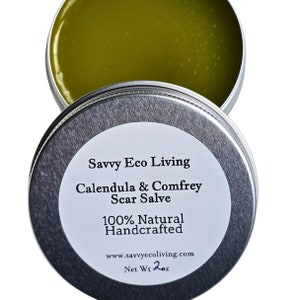 May include: A silver tin with a white label that reads "Savvy Eco Living Calendula & Comfrey Scar Salve 100% Natural Handcrafted www.savvyecoliving.com Net Wt 2oz". The tin contains a green salve.