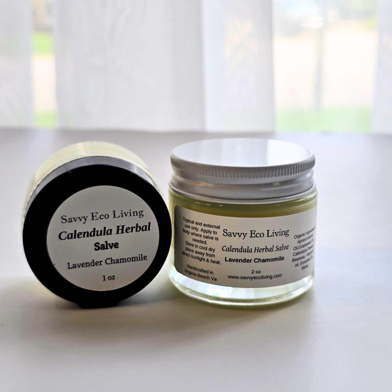 May include: Two clear glass jars of Savvy Eco Living Calendula Herbal Salve with Lavender Chamomile. One jar has a black lid and a 1 oz label, while the other has a white lid and a 2 oz label. Both feature white labels with black text.