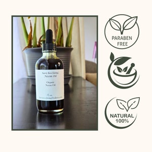 以下が含まれることがあります： ドロップ式の有機ニームオイルのボトル（118ml）。ボトルには「Savvy Eco Living Neem Oil」とラベルが貼られています。ラベルには、オイルがオーガニックであることと、会社のメールアドレスが記載されています。ボトルは暗い木製のテーブルの上に置かれています。画像には、「Paraben Free」、「Natural 100%」と書かれた緑と白のラベルが3つと、葉のついた乳鉢と乳棒も写っています。