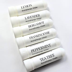 May include: A collection of white aromatherapy inhalers, each labeled with a different essential oil: Lemon, Lavender, Bergamot, Frankincense, Peppermint, and Tea Tree. The text "Aromatherapy Inhaler" is printed below each oil name.