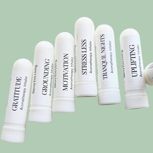 May include: A collection of white aromatherapy inhalers with various labels, including "Gratitude," "Grounding," "Motivation," "Stress Less," "Tranquil Nights," and "Uplifting." Each inhaler has black text and is labeled "Savvy Eco Living."