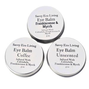 May include: Three silver tins of Savvy Eco Living eye balm. The tins are labeled with the product name, "Eye Balm", and the scent: "Frankincense & Myrrh", "Coffee", and "Unscented". Each tin is 0.5 ounces.