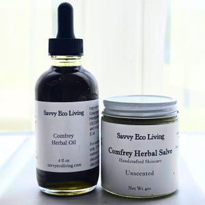 May include: A 4 fl oz glass bottle of Savvy Eco Living Comfrey Herbal Oil with a black dropper cap and a white label, alongside a jar of Savvy Eco Living Comfrey Herbal Salve with a white lid and a white label marked as 4 oz net weight.