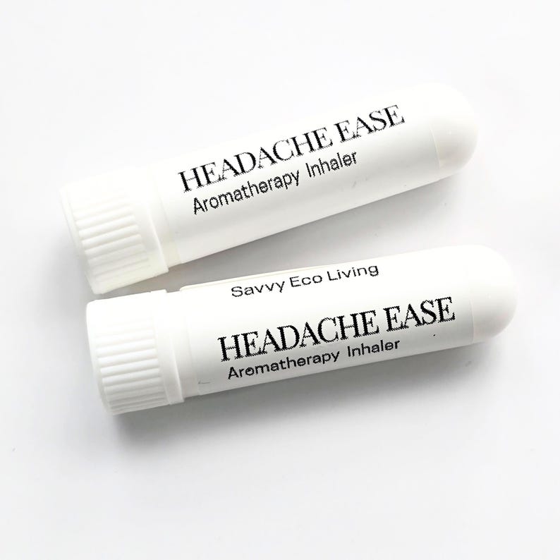 K&ouml;nnte beinhalten: Zwei wei&szlig;e Aromatherapie-Inhalatoren mit dem Text "HEADACHE EASE" und "Aromatherapy Inhaler" in Schwarz aufgedruckt. Ein Inhalator tr&auml;gt auch den Text "Savvy Eco Living". Die Inhalatoren haben eine zylindrische Form mit geriffelter Kappe.