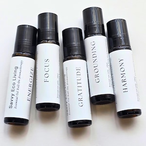 May include: Five essential oil roll-on bottles with black caps and white labels. The labels read "ENERGIZE", "FOCUS", "GRATITUDE", "GROUNDING", and "HARMONY". The bottles are labeled "Savvy Eco Living Essential Oil Roll-On Aromatherapy".