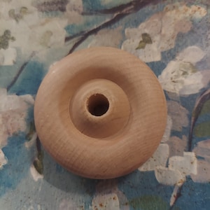 May include: A plain wooden wheel with a hole in the center. The wheel is light brown and has a smooth surface.