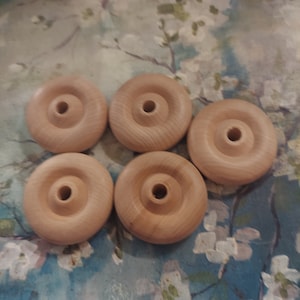 May include: Five unfinished wooden wheels with a hole in the center. The wheels are light brown and have a smooth surface.