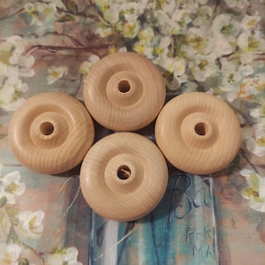 May include: Four unfinished wooden wheels with a hole in the center. The wheels are arranged in a circle on a floral patterned surface.