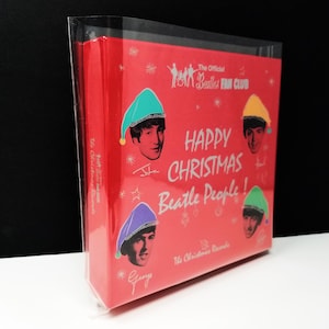 May include: A red box set featuring The Beatles with the text "Happy Christmas Beatle People!" and the words "The Christmas Records." The box has images of the band members wearing Christmas hats. The Official Beatles Fan Club is also printed on the box.
