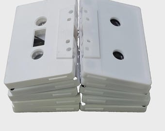 May include: A stack of white plastic audio cassette tapes with visible magnetic tape reels and central hubs. The rectangular cassettes feature a smooth white shell with a rectangular window and two circular openings for the tape spools.