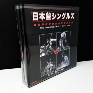 Puede incluir: Un box set negro titulado "The Japanese Singles 1978-1984" con imágenes de una banda actuando. El texto "日本盤シングルズ" se muestra en rojo y blanco. El box set está etiquetado 45RPM.