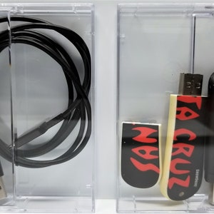 May include: Two clear plastic cases containing various USB drives. The first case contains a black USB cable. The second case contains three USB drives: one black with "Cruzer Glide 16GB" text, one white with "Santa Cruz" text in red, and one black with a red flame design.