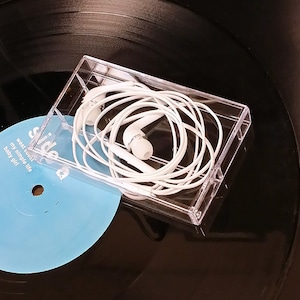 May include: White wired earphones in a clear plastic case on top of a black vinyl record with a blue label that says "side a" and "west coast my simple life baby girl".