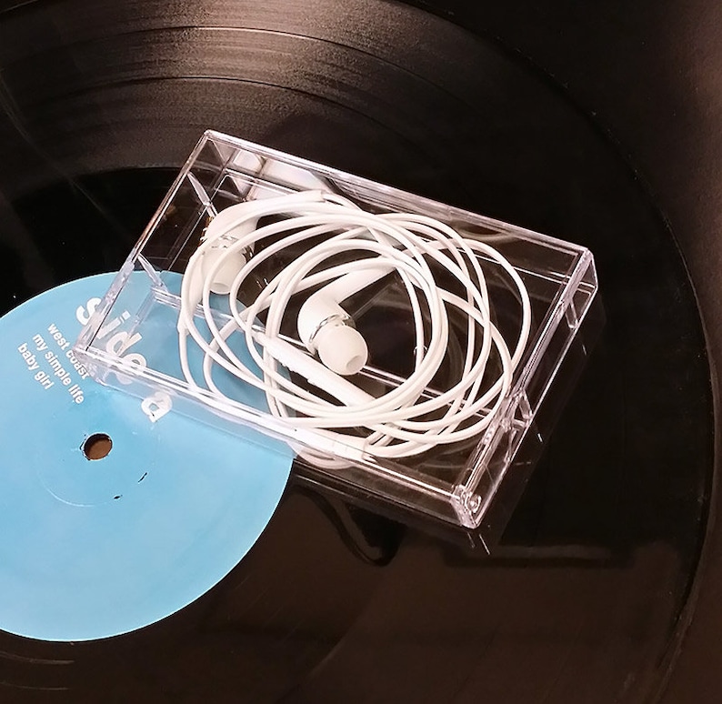 May include: White wired earphones in a clear plastic case on top of a black vinyl record with a blue label that says "side a" and "west coast my simple life baby girl".