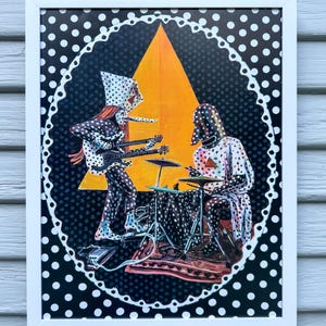 May include: A framed art print featuring two figures in polka-dot outfits playing music. One figure plays a double-neck guitar, while the other plays drums. They are set against a large yellow triangle on a black background with white polka dots.