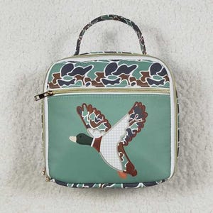 May include: Green lunch bag with a duck applique. The bag features a camouflage pattern on the top and handle, a gold zipper, and a white border. The duck has brown, green, and white wings, and a checkered pattern.