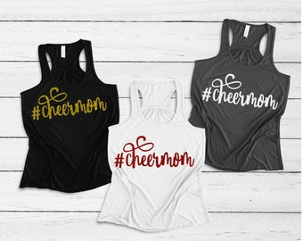 May include: Three tank tops with the text "#cheermom" in different colours and fonts. The tank tops are black, white and grey.