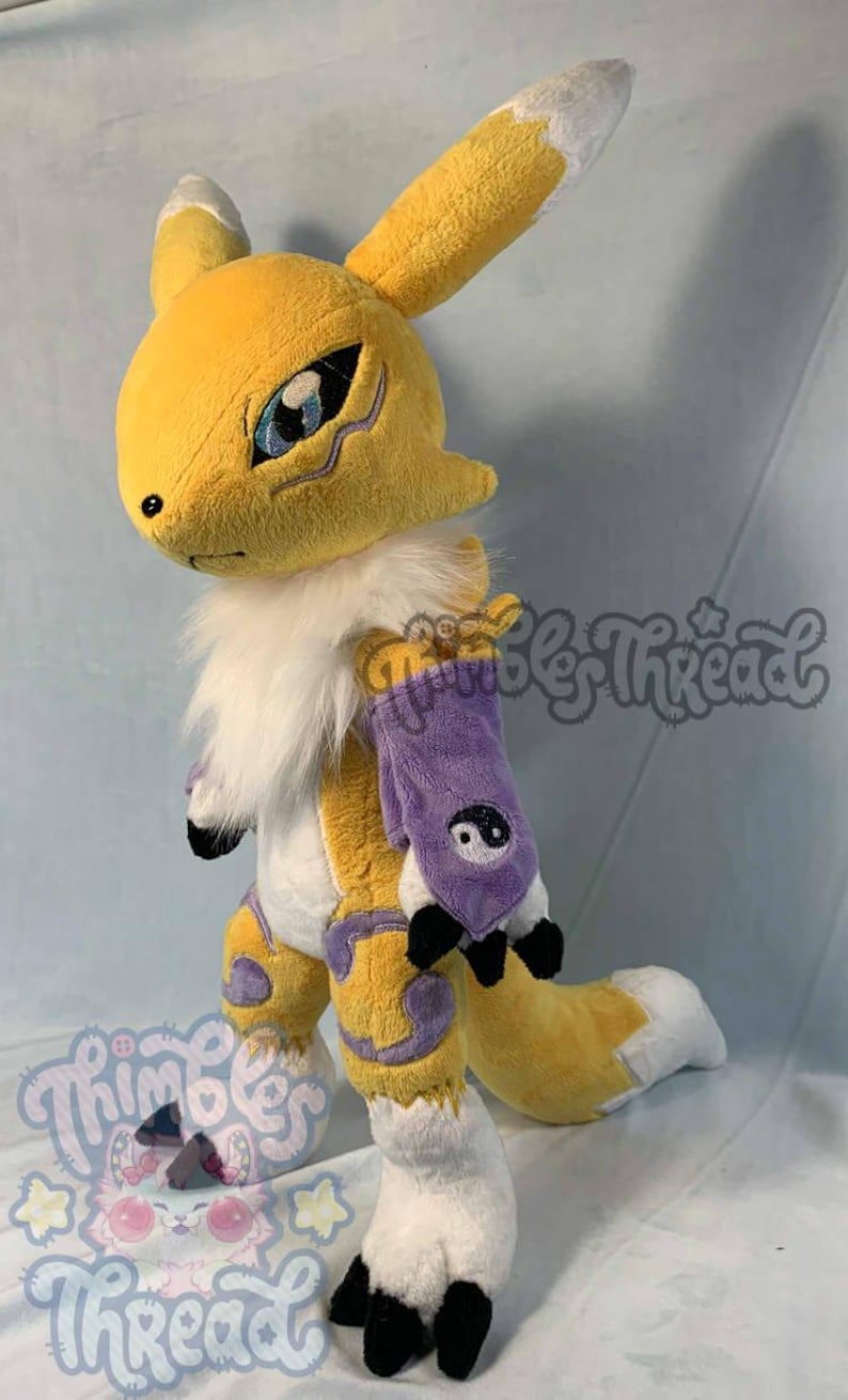 May include: A plush toy of a yellow fox-like creature with white accents, large ears, and a fluffy white collar. It has a purple arm sleeve with a yin-yang symbol and black claws. The toy is handmade.