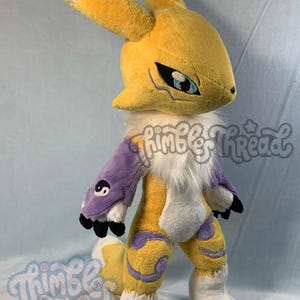 May include: A plush toy of a yellow and white creature with large ears, purple accents, and black claws. The toy has blue eyes and a white fluffy chest. The Thimble Thread logo is visible on the image.