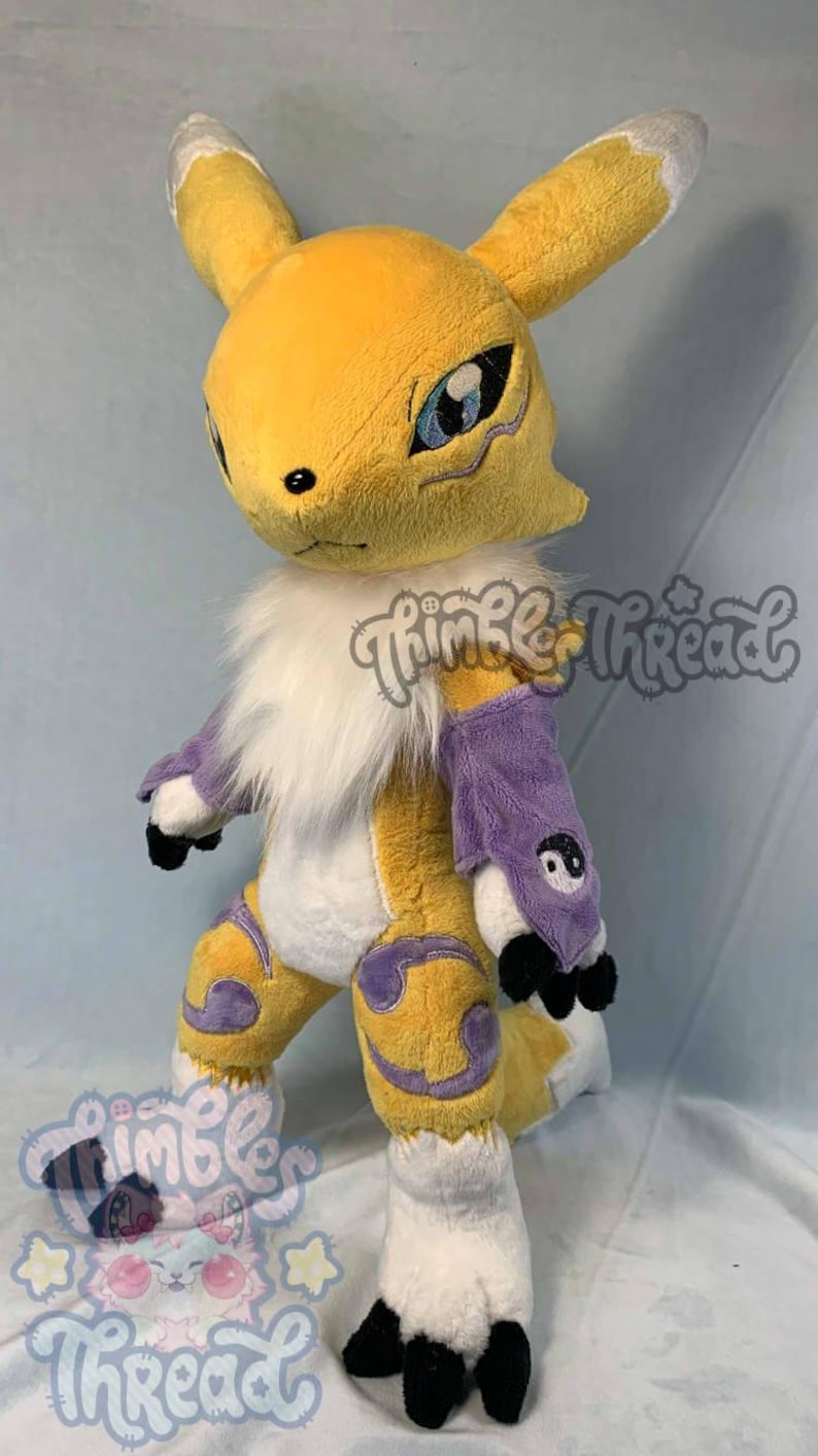 May include: A plush toy of a yellow fox-like creature with white and purple accents. The toy has large ears, blue eyes, and black claws. The text "Thimble Thread" is visible on the image.