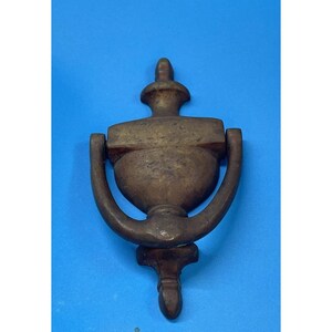 May include: A vintage brass door knocker with a classic urn design. The knocker features a curved handle and a decorative finial at the top. The brass has a warm, aged patina, suggesting its antique nature. The knocker is mounted on a blue background.
