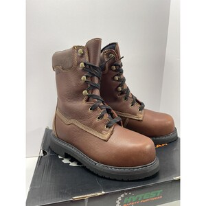 May include: A pair of brown leather work boots with black laces and brass eyelets. The boots have a padded collar and a black sole. The boots are sitting on a black and white box with the words "HYTEST SAFETY FOOTWEAR".